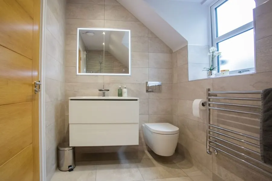 Modern beige bathroom with floating vanity, wall mirror, toilet, towel warmer, and window light