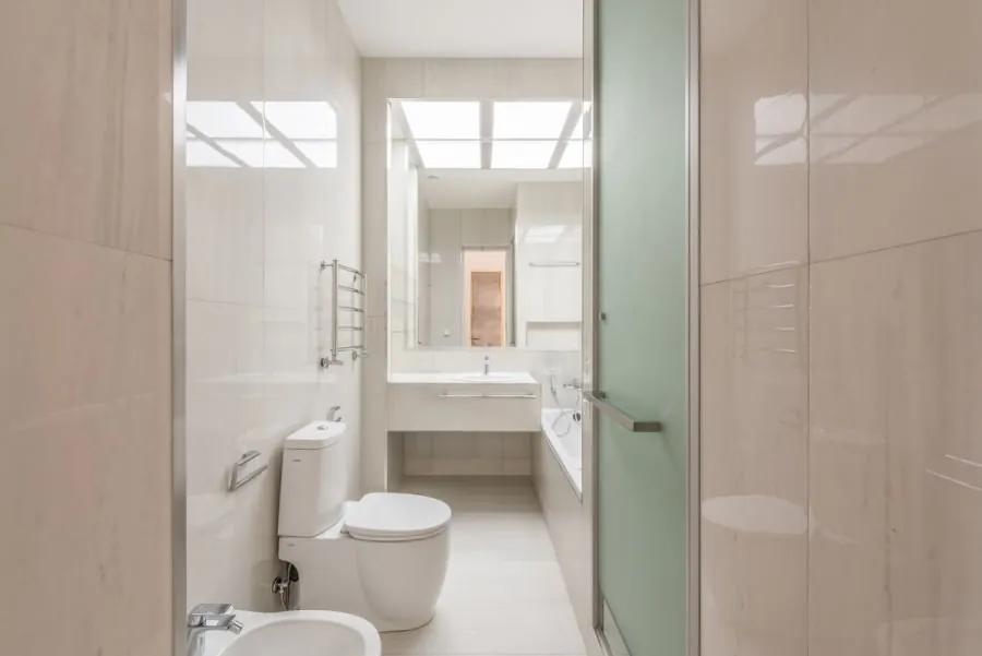 Bright tiled bathroom with toilet, sink, shower, and frosted glass door.