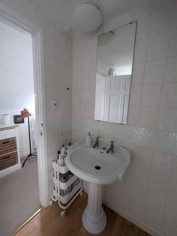 White bathroom with sink, mirror, and a small rolling cart.