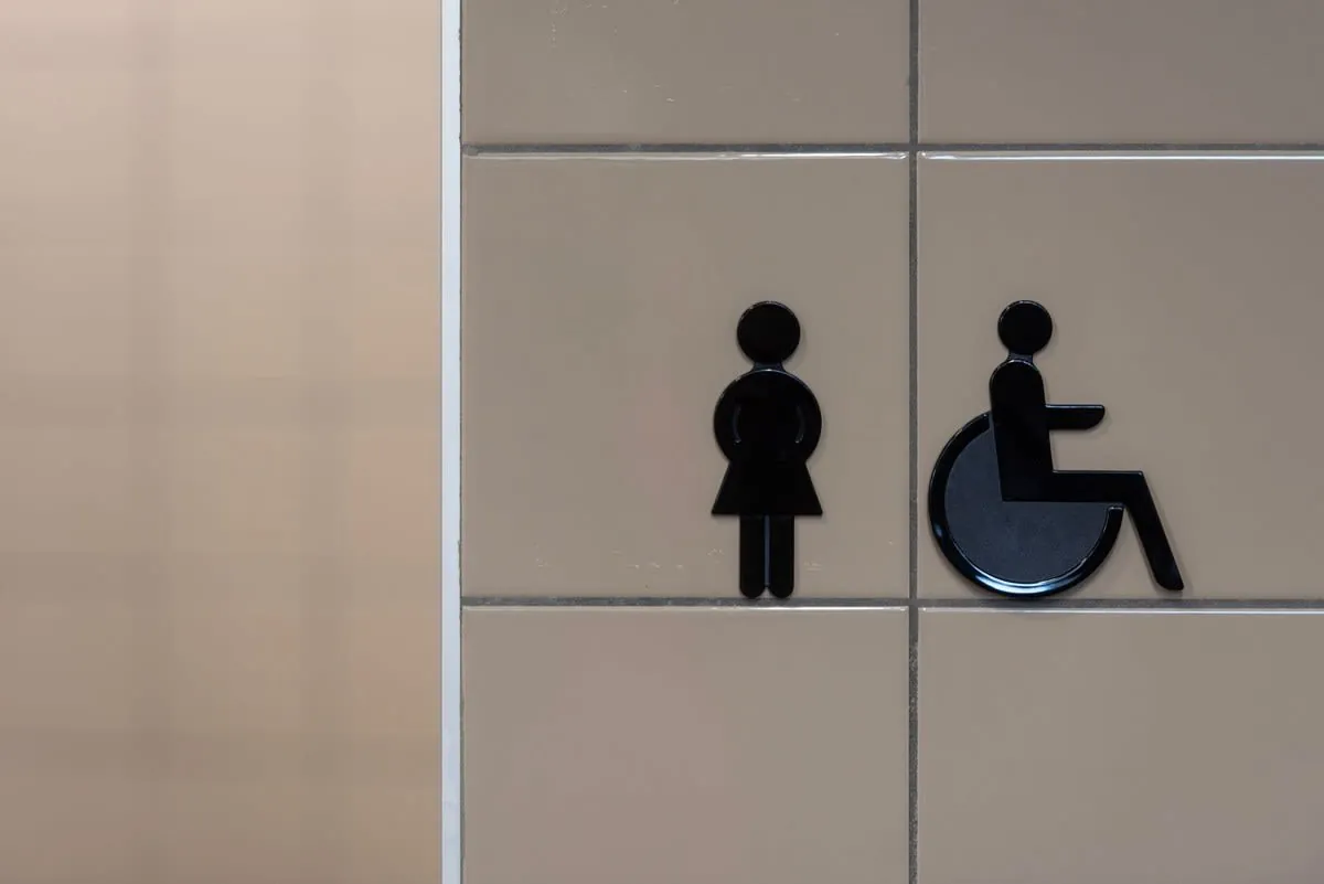 Female and wheelchair accessibility restroom signs on beige wall tiles