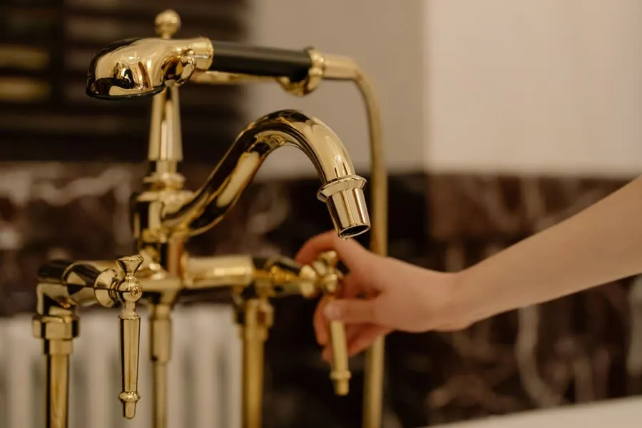 Hand reaching for a gold bathroom faucet in a sink area