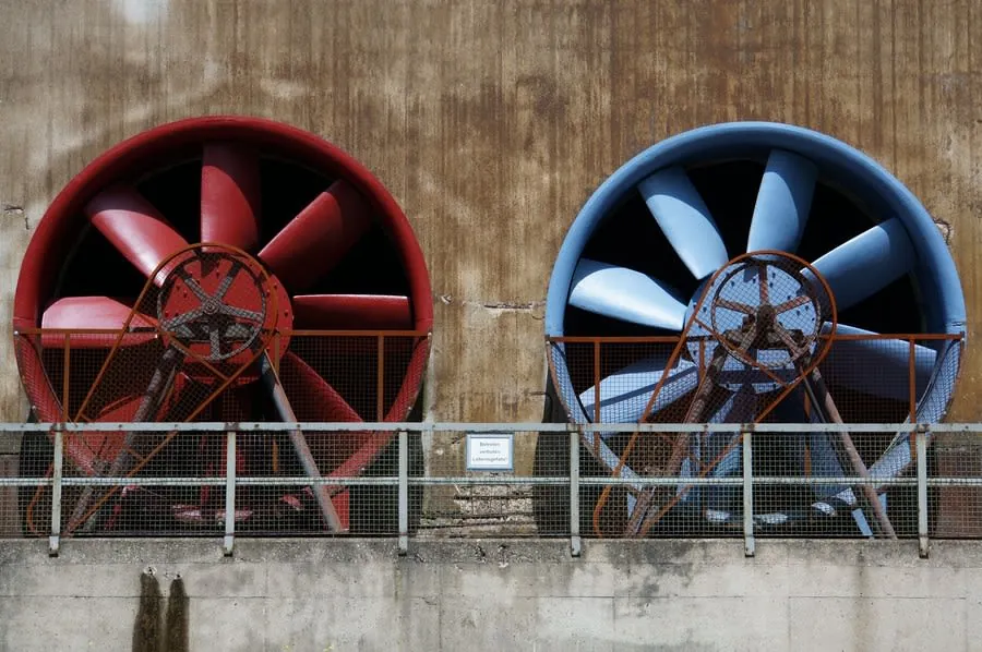 Two large industrial fans, one red and one blue, mounted on a concrete wall.