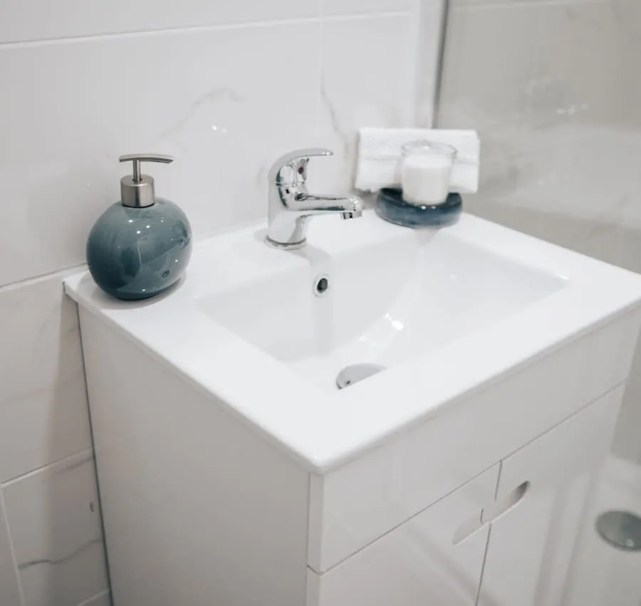 White bathroom sink with chrome faucet, blue soap dispenser, and candle on the counter