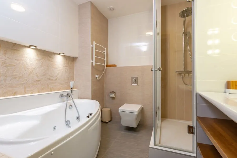 Modern bathroom with white corner tub, glass shower, wall-mounted toilet, and beige tile.