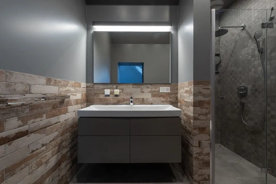 Modern bathroom with floating vanity, large mirror, stone tile walls, and glass shower.