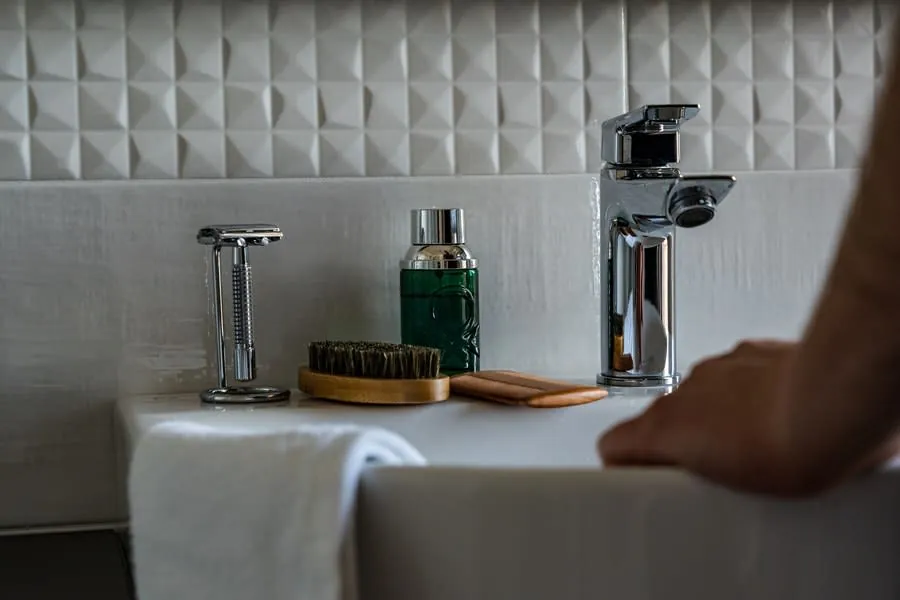 Bathroom sink with toothbrush, green bottle, and soap, with a person’s arm at the right edge
