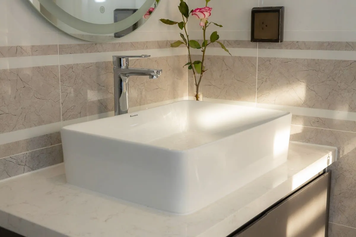 Modern bathroom with a white countertop sink, chrome faucet, mirror, and a small vase of flowers