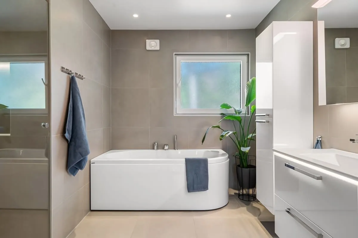 Modern bathroom with freestanding tub, gray tile walls, white vanity, and a small window