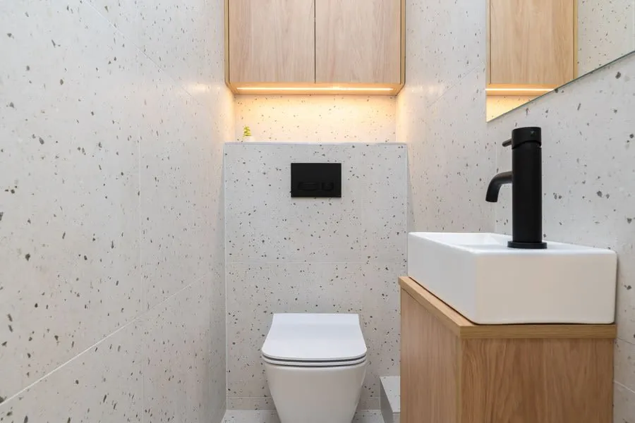 Compact modern bathroom with toilet, wall-mounted sink, black faucet, and wood cabinetry