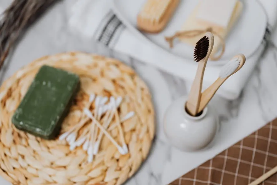 Green soap bar, cotton swabs, and woven trays on a marble bathroom counter.
