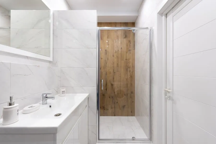 Modern white bathroom with vanity, mirror, tiled shower, and wood-look shower door