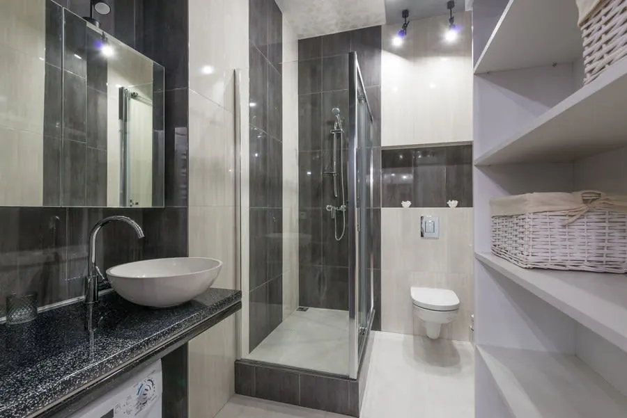 Modern gray bathroom with glass shower, vessel sink, toilet, and open shelving