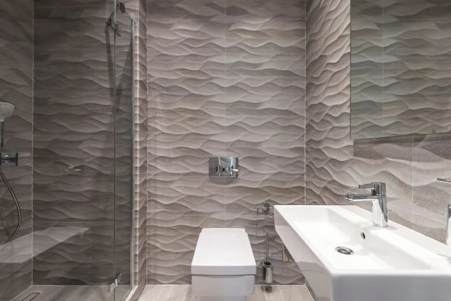 Modern bathroom with textured gray tile, wall-mounted toilet, and white sink vanity