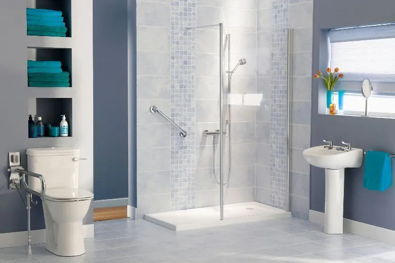 Modern bathroom with glass shower, toilet, pedestal sink, and blue accents