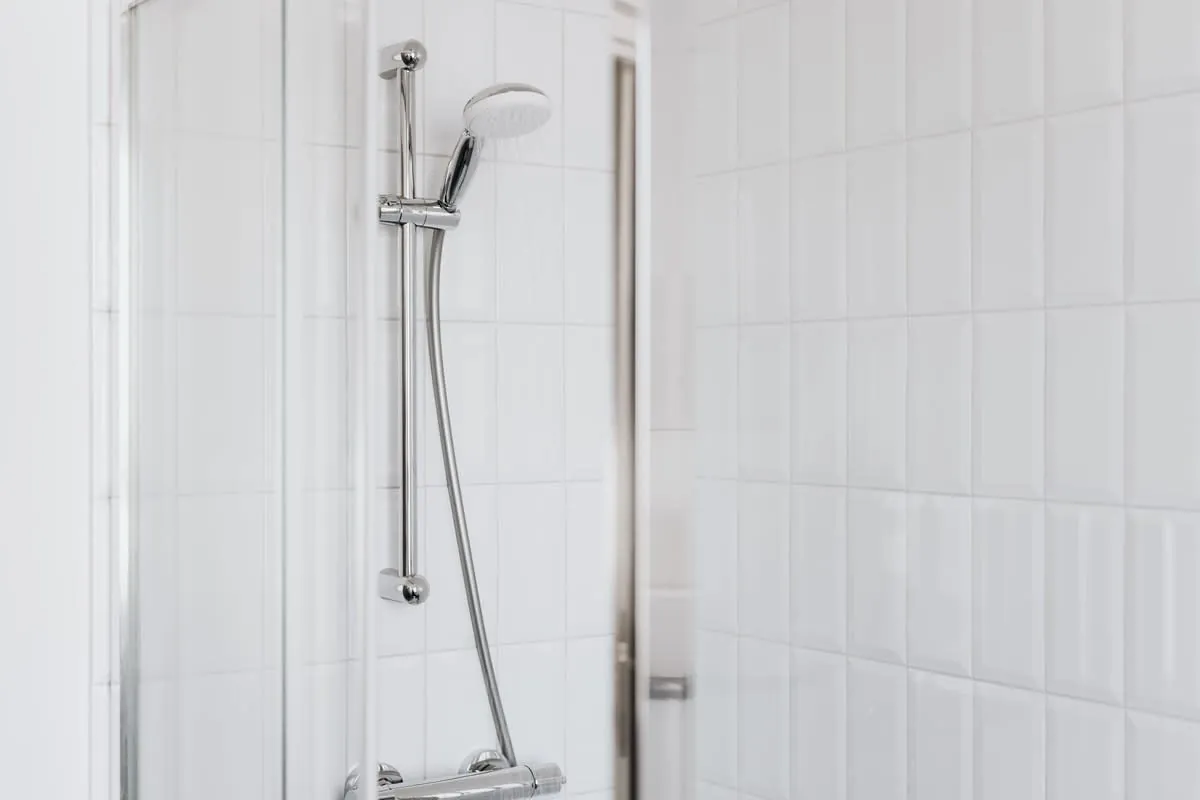 White tiled shower with chrome handheld showerhead and vertical grab bar
