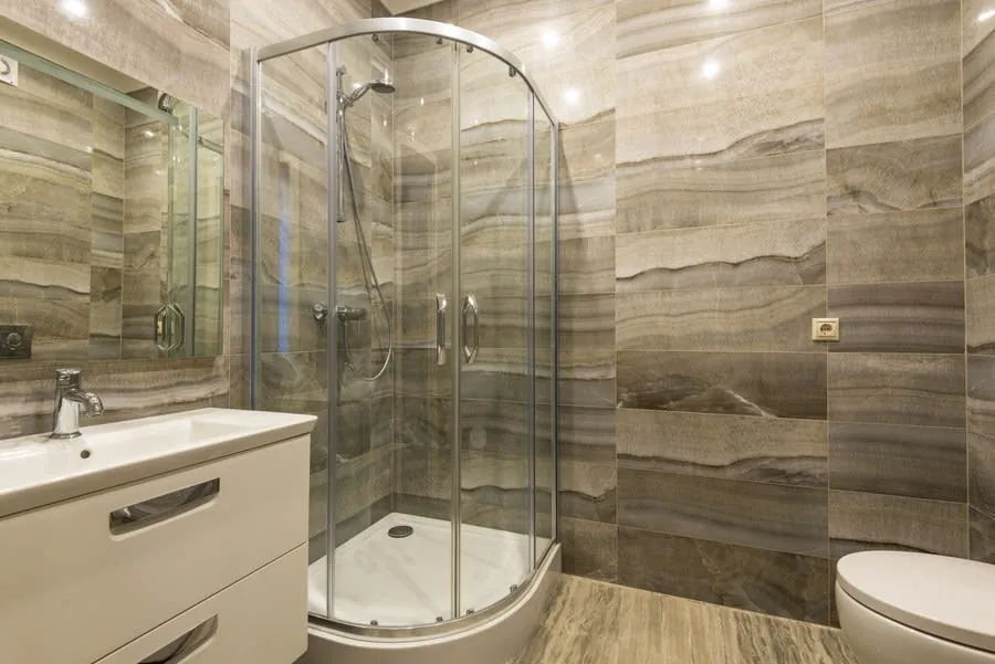 Modern bathroom with glass shower, white vanity, and beige stone tile walls