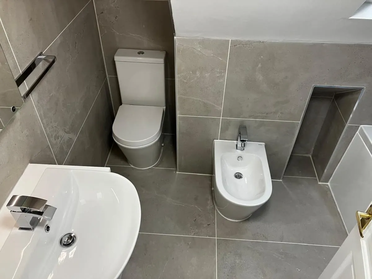 Modern gray-tiled bathroom with toilet, sink, bidet, and walk-in shower area