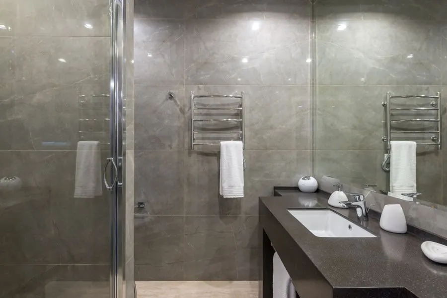 Modern bathroom with gray tiled walls, glass shower, and dark vanity with sink and towel rack.