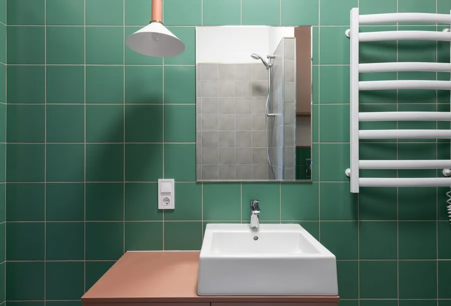 Green-tiled bathroom with sink, mirror, lamp, and white towel radiator