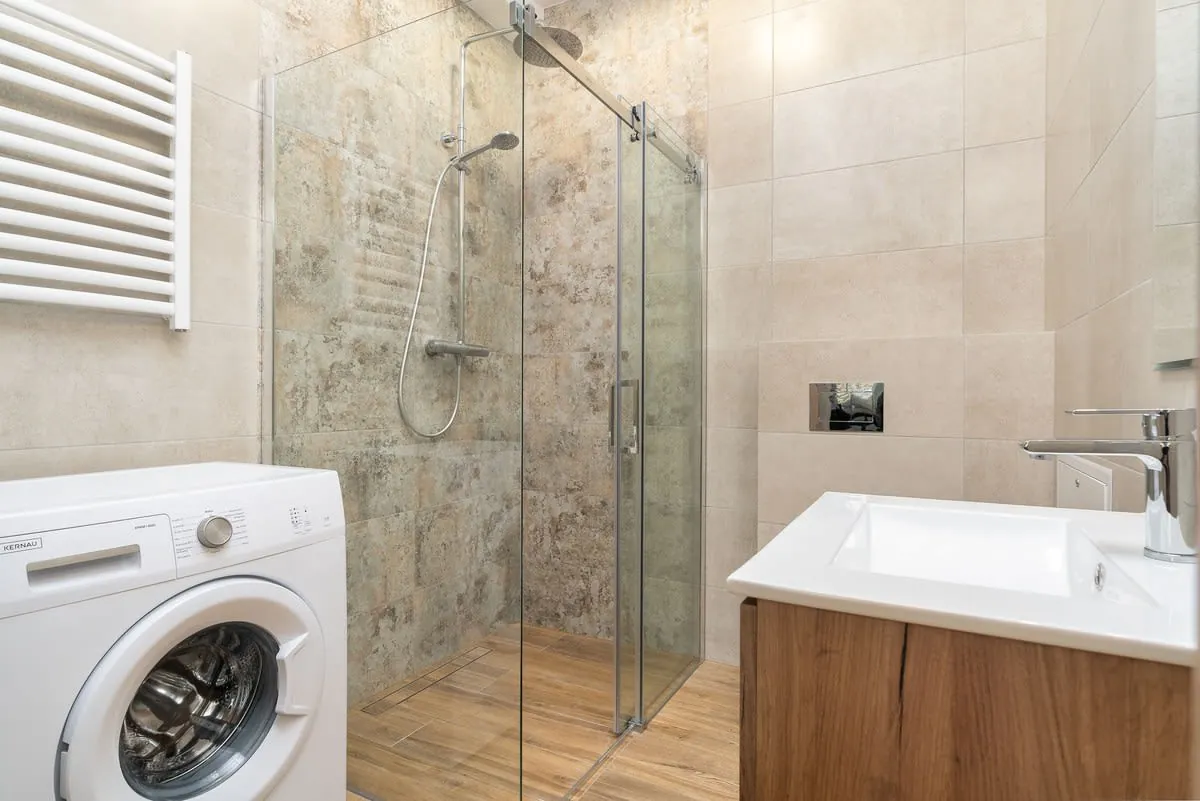 Modern bathroom with shower, sink, and washing machine on wood-look tile floor