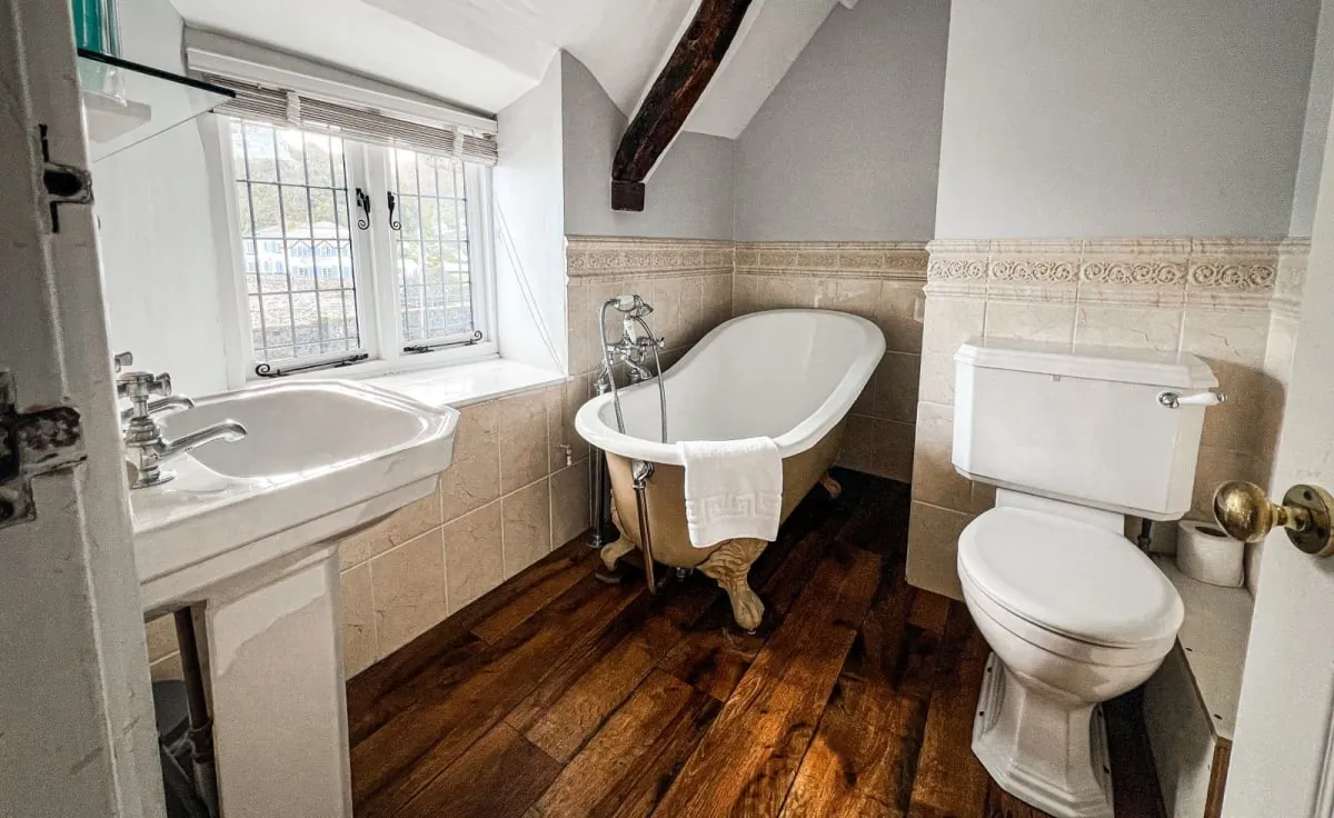 Small bathroom with a clawfoot tub, toilet, sink, and wood floor under a window.
