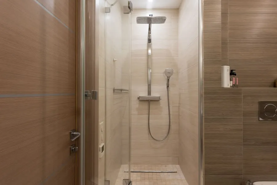 Small tiled bathroom shower with glass doors, chrome rainfall showerhead, and a hand-held shower sprayer.