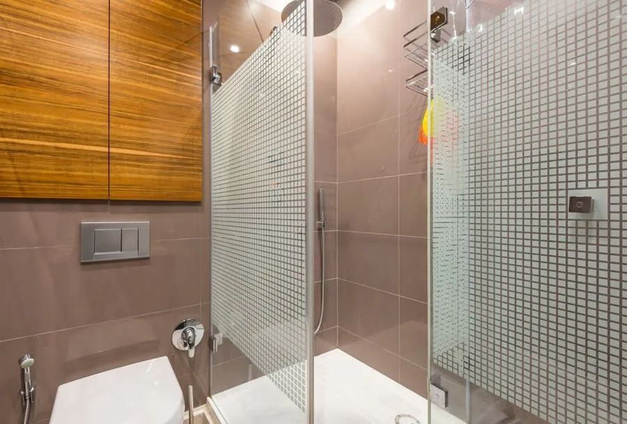 Modern bathroom with glass shower, pink tile walls, wood cabinet, and toilet edge visible