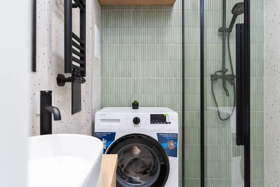 Compact washer in a small modern bathroom beside a shower and sink.