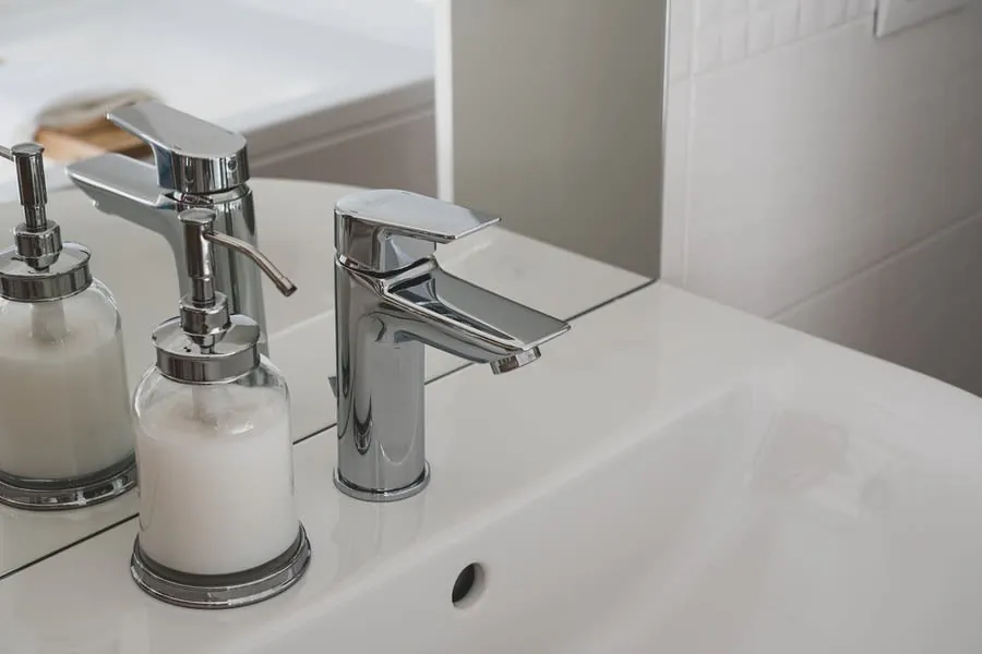 Chrome bathroom sink faucet with two glass soap dispensers on a white countertop