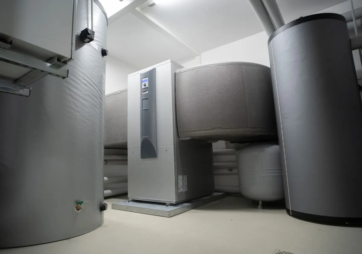Industrial equipment room with large gray tanks, pipes, and a central silver appliance.