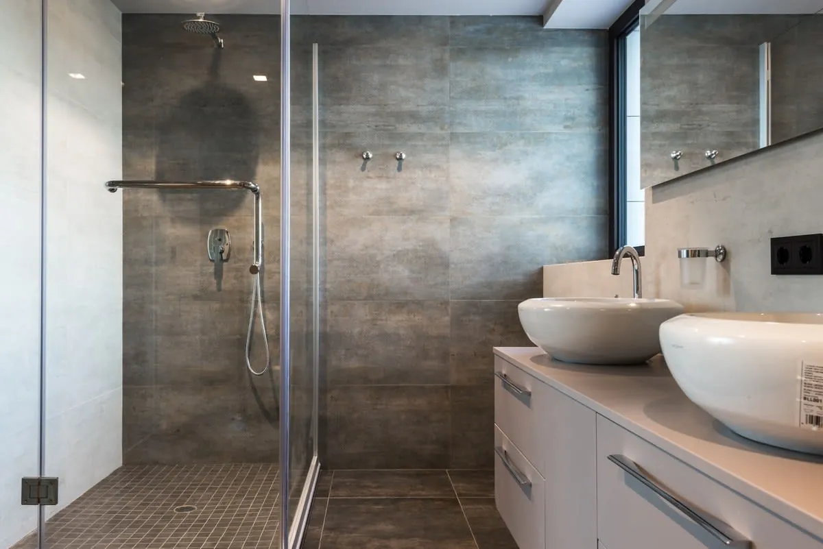 Modern bathroom with walk-in shower, double sinks, gray tile, and glass partition