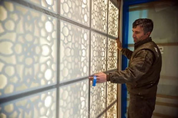 Man installing a decorative panel with a floral-like pattern. The panel has white, openwork designs, framed in dark lines.