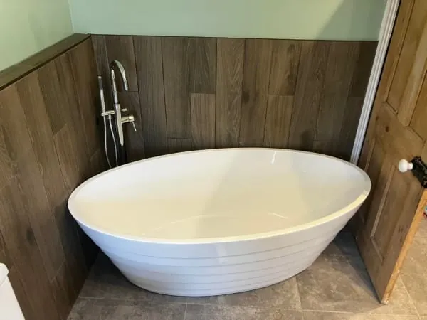 White oval bathtub against wood-paneled wall with a faucet and partially open wooden door.