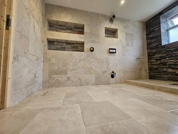 Stone-tiled shower room with recessed shelves, a window on the right, and a partly built-in space on the floor.