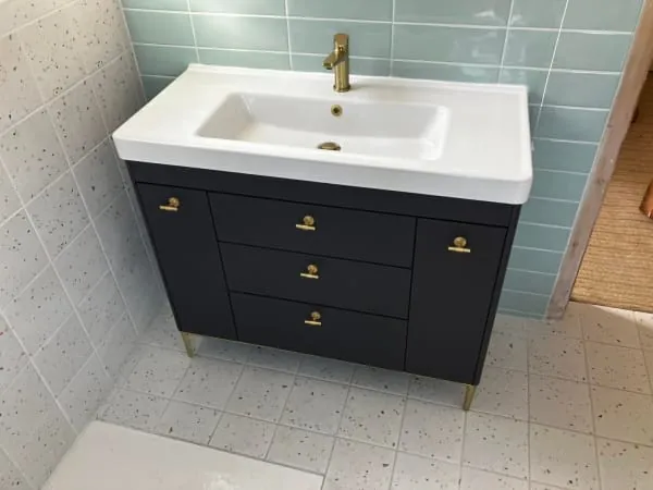 Bathroom vanity with dark gray cabinet, white sink, gold fixtures, and tile backsplash.