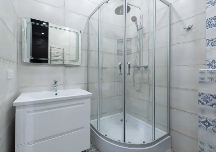 Bathroom with white vanity, glass shower, and tiled walls.