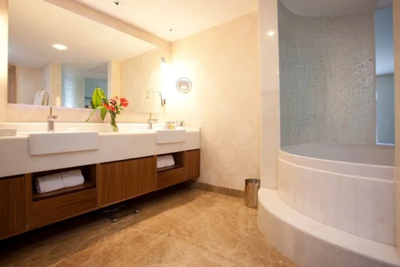 Luxurious bathroom with marble floor, double sinks, wood cabinetry, and a rounded shower.