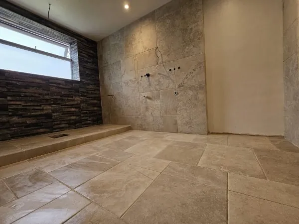 Bathroom interior with stone tiles on floor, window, and wall. Recessed lighting.