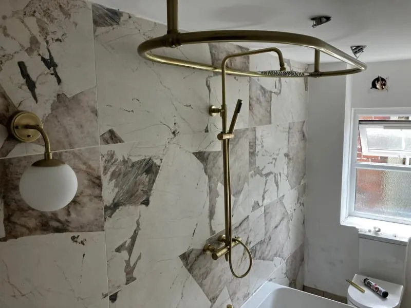 A bathroom with a marble-tiled shower, brass fixtures, and a globe-shaped wall light.