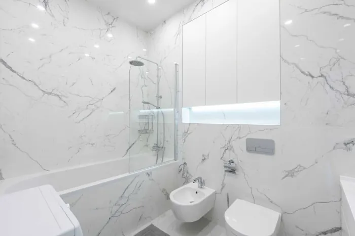 White marble bathroom with tub, shower, toilet, bidet, and storage cabinet.