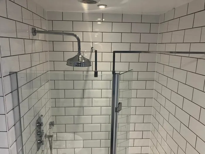 White tiled shower with glass door and chrome shower head and fixtures.