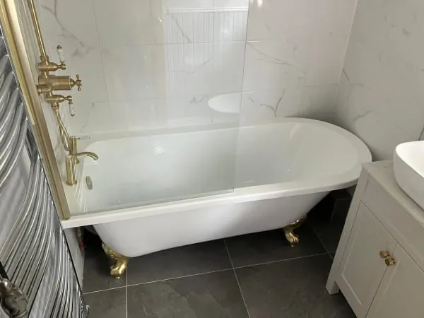 Claw-foot bathtub with gold fixtures, marble tile, and white vanity in a modern bathroom.