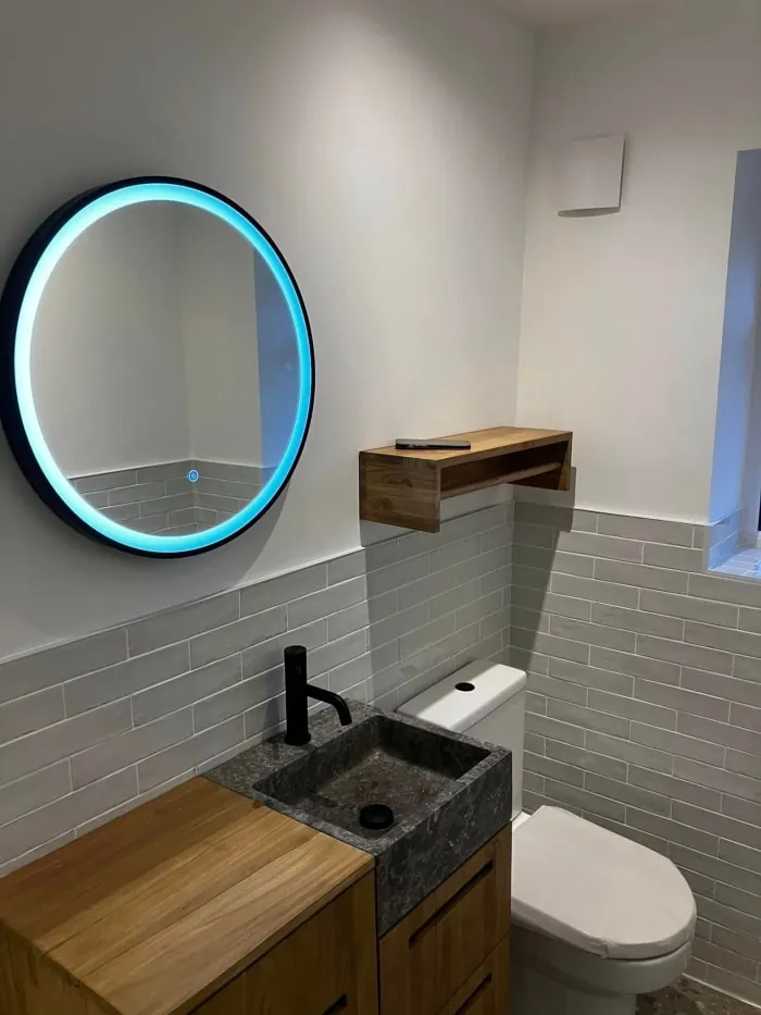 Small modern bathroom with a round mirror, wooden vanity, and toilet.