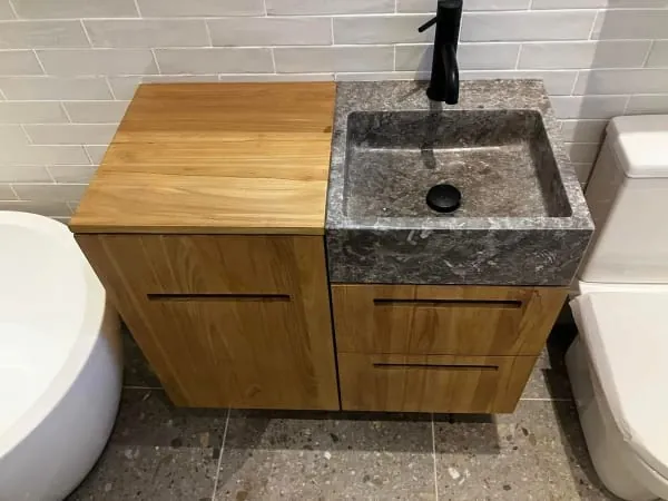 Wooden bathroom vanity with gray stone sink, black faucet, and toilet.