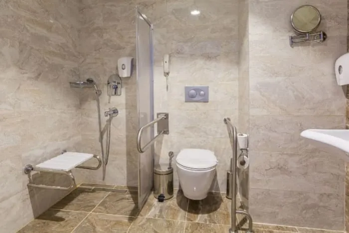 Accessible bathroom with shower, toilet, and sink; handrails and a shower seat are visible.