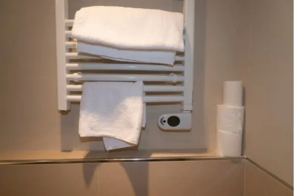 White towels on a heated rack in a bathroom next to toilet paper rolls.